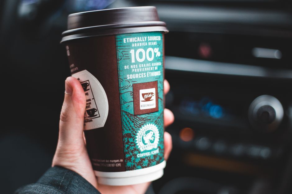 Closeup of faceless guy with disposable cup of hot coffee to go in hand sitting in car