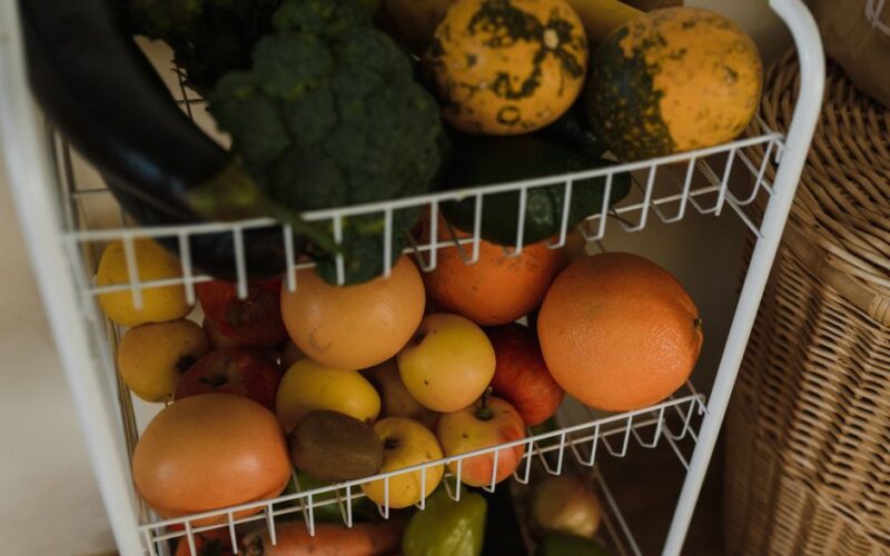 Colorful assortment of fruits and vegetables displayed on a wire shelf in a home setting.
