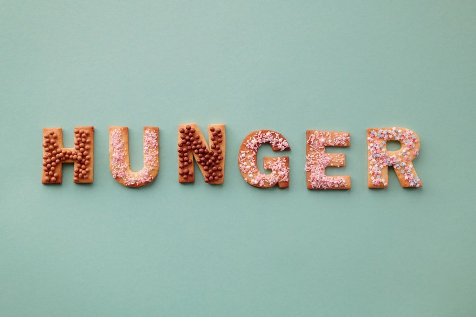 Colorful cookies spelling the word 'Hunger' on a pastel background, topped with sprinkles.