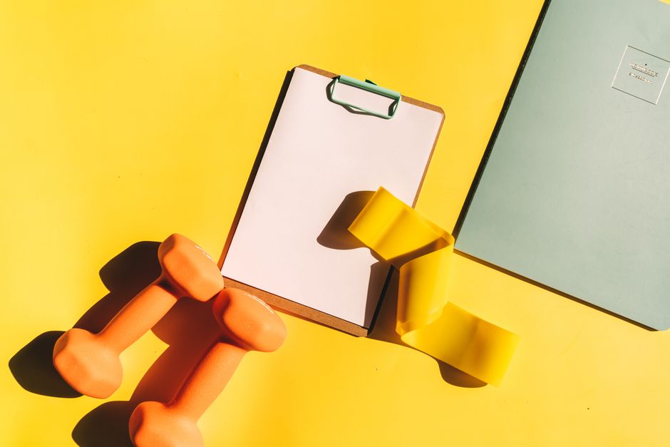 Colorful fitness setup with dumbbells, clipboard, and push straps on a vibrant background.