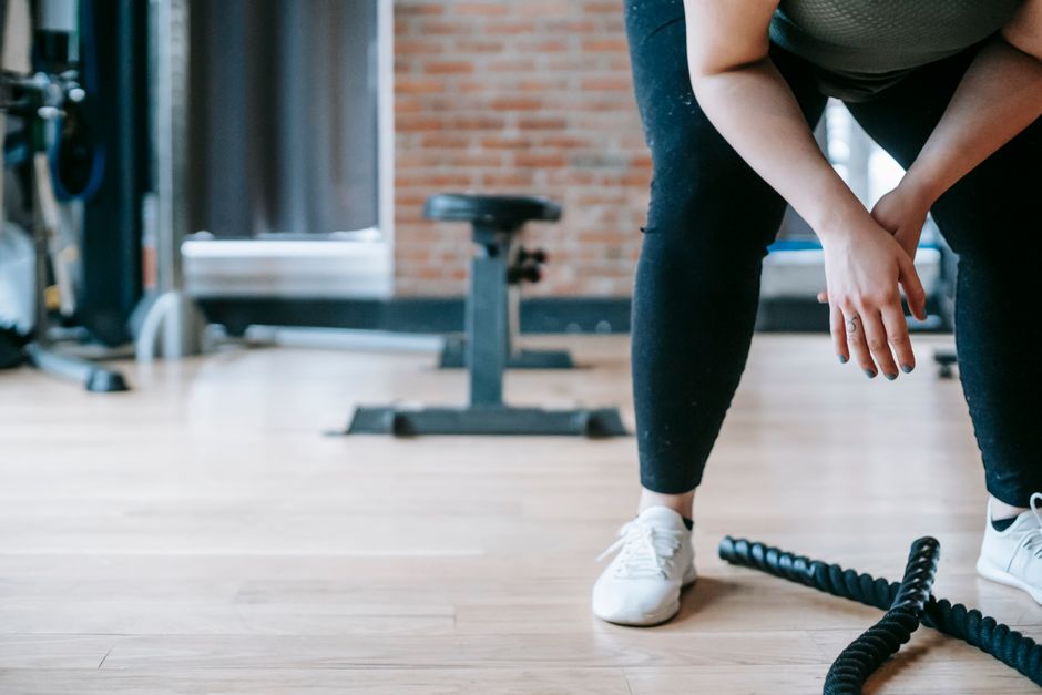 Crop anonymous female in sportswear resting after workout with ropes in gym with sports equipment