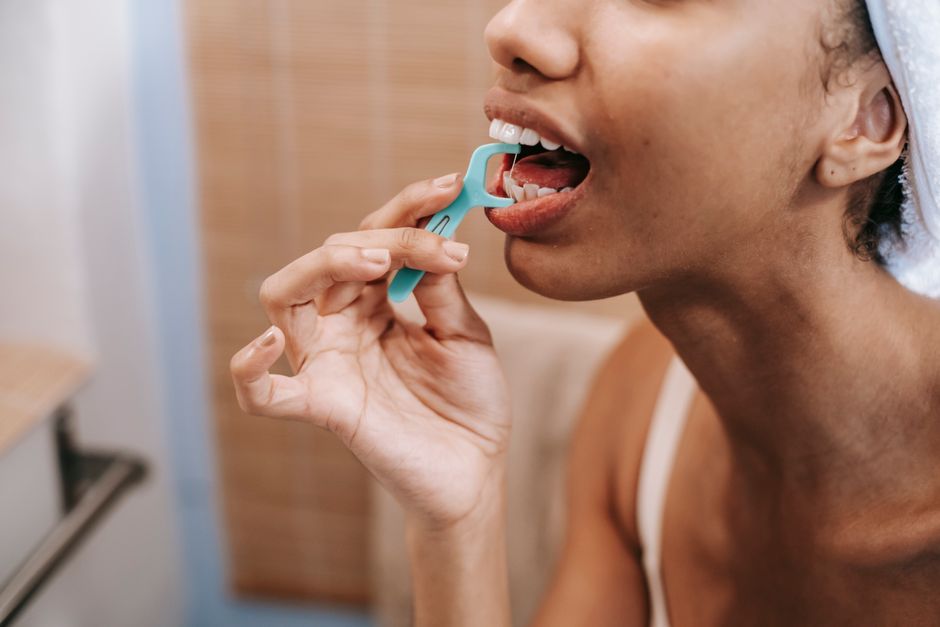 Crop ethnic female doing oral procedure with dental flosser in morning at home