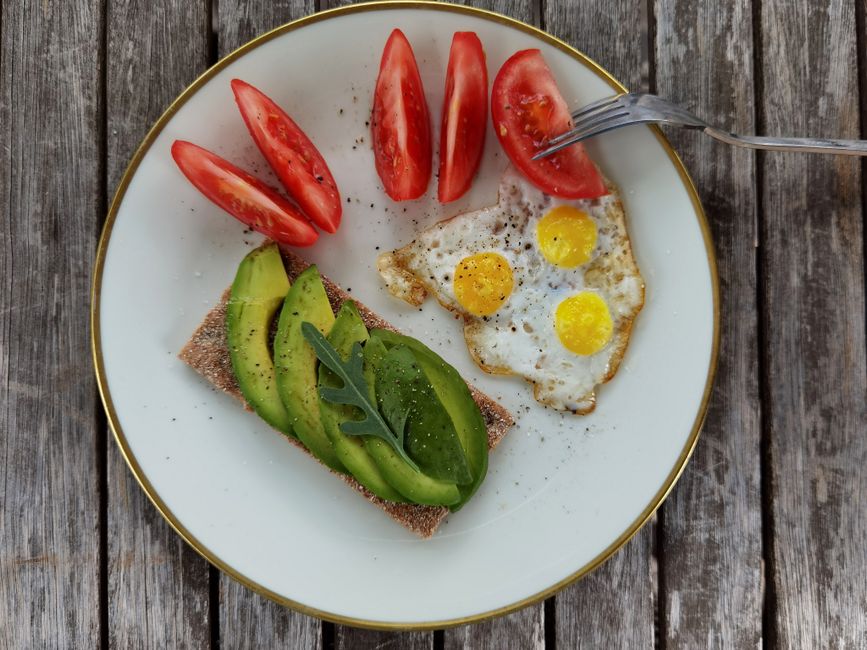 Delicious breakfast plate with sliced avocado, tomatoes, and sunny-side-up quail eggs.
