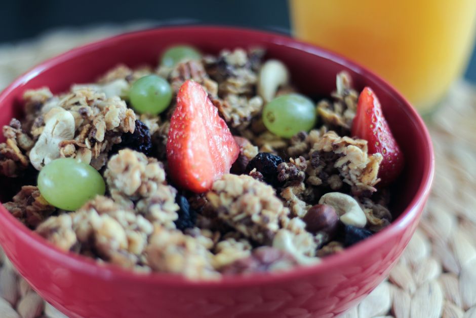 Delicious muesli topped with fresh strawberries, grapes, and assorted nuts in a red bowl.