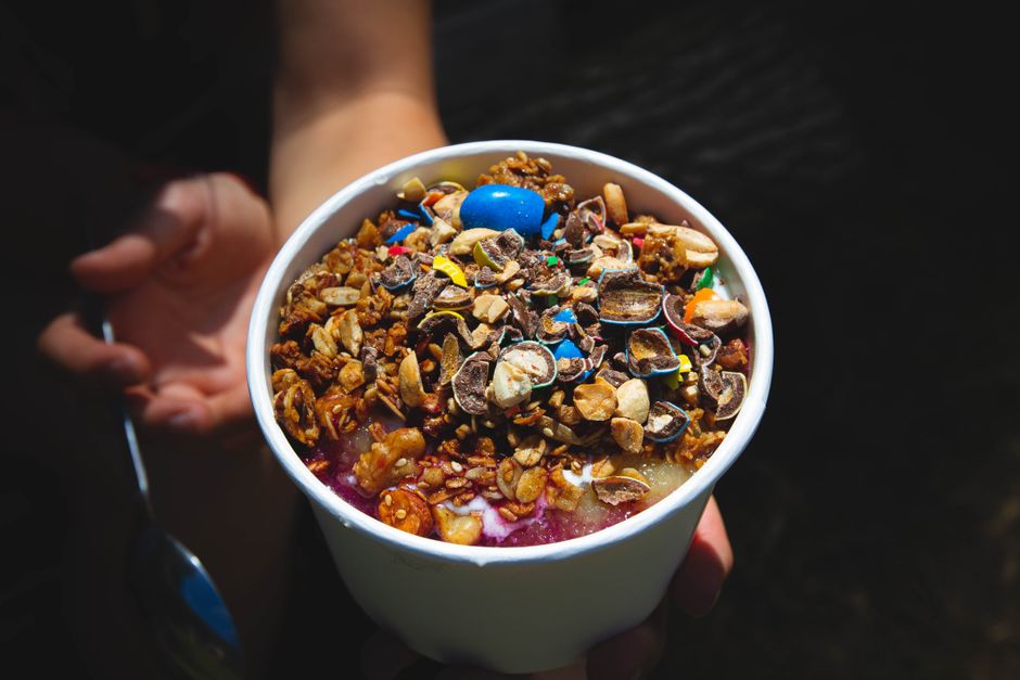 Delicious smoothie bowl topped with granola and chocolates in a white bowl.