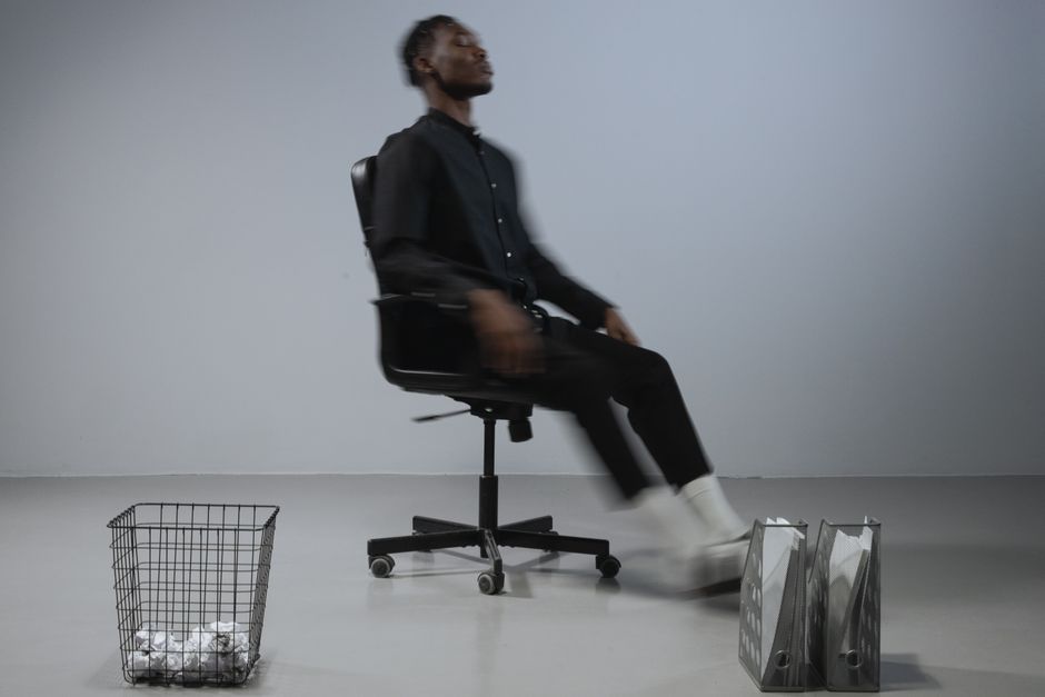 Dynamic office scene with blurred motion of man on chair, files and trash bin in focus.