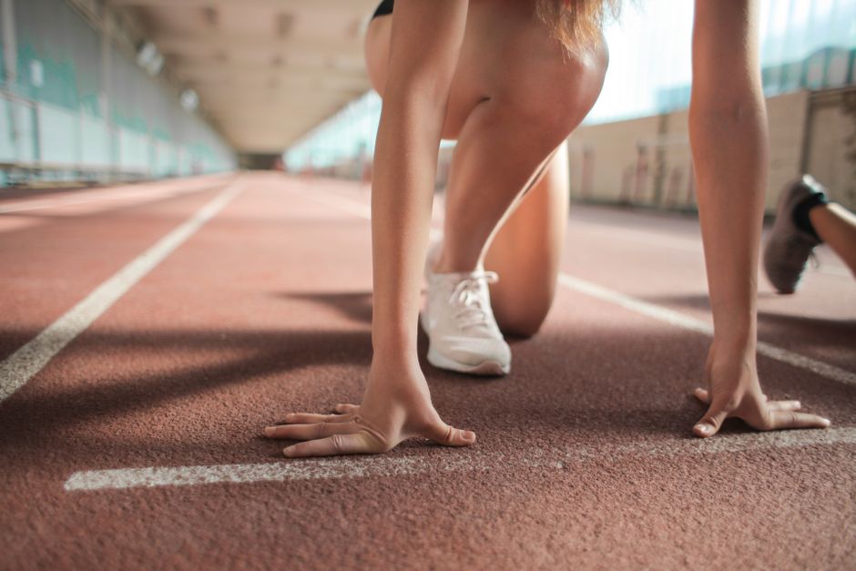 Faceless female sprinter in running crouch start pose putting hands on starting line on track