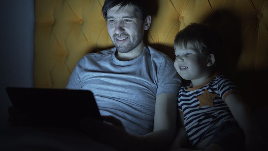 Father and son bonding, watching tablet in dim light, evening routine.