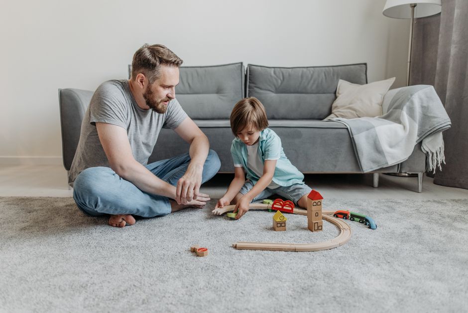 Father and son enjoying quality time playing with a wooden toy train set on the living room floor.