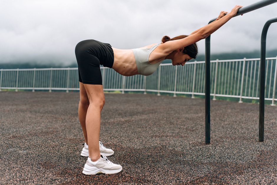 Fit woman stretching on outdoor gym equipment under cloudy skies, promoting active lifestyle.