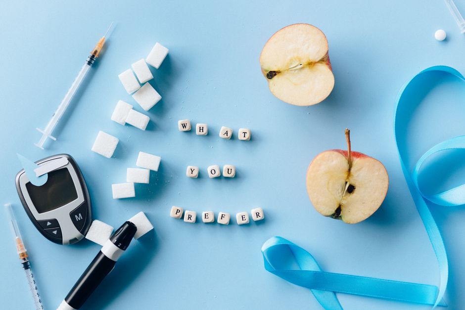 Flat lay of diabetes awareness theme with glucometer, syringe, sugar, and apple on blue background.