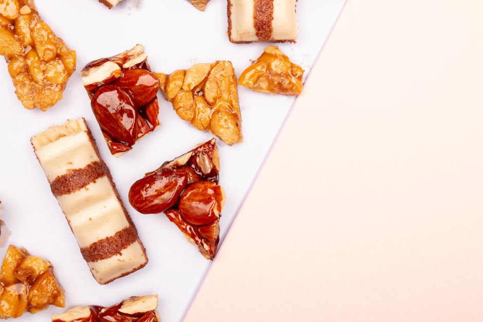 Flat lay of gourmet sweets, nougat, and nut brittle on a pastel background. Perfect for dessert lovers.