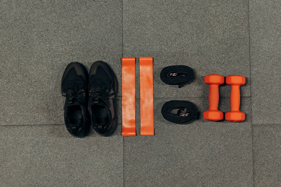 Flat lay of gym essentials including dumbbells, sneakers, and resistance bands on a grey floor.