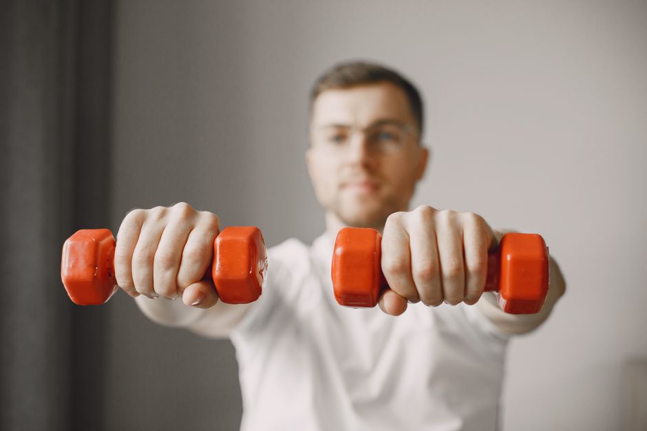Focused adult male exercising with red dumbbells at home, promoting a healthy lifestyle.