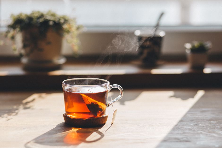 Glass teacup with steaming tea catching warm sunlight, indoors by the window.
