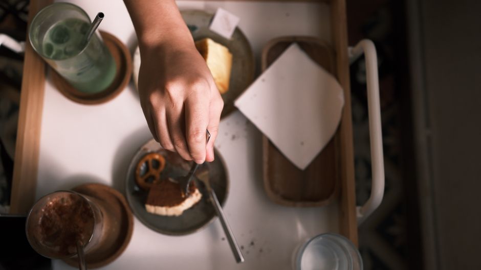 Hand reaching for a dessert with drinks and snacks on a tray, perfect for lifestyle and food themes.