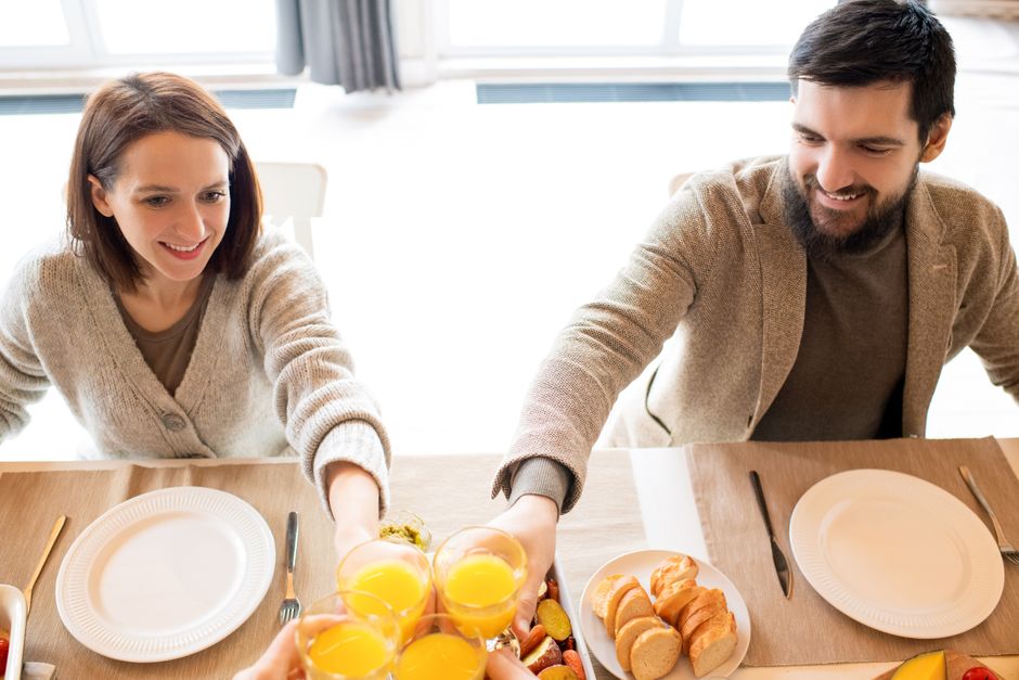Happy couple toasting with orange juice during breakfast at home.