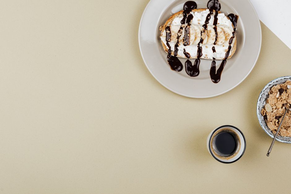 High-angle view of dessert with chocolate syrup, cereals, and coffee on a flat, beige background.