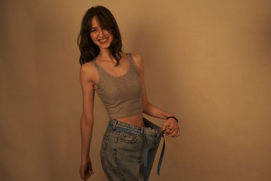 Joyful woman shows success in weight loss by wearing loose jeans. Healthy lifestyle concept.