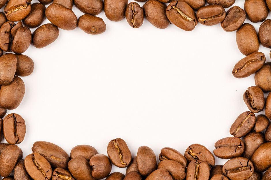 Macro photography of brown coffee beans framing a white background, showcasing freshness and texture.