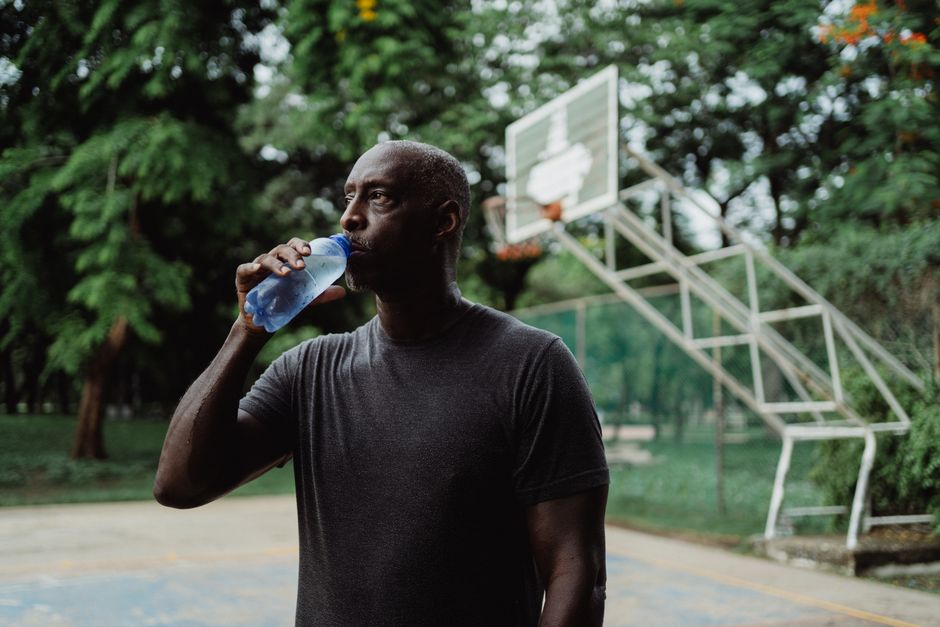 Man drinking water on a basketball court surrounded by trees, enjoying a break.