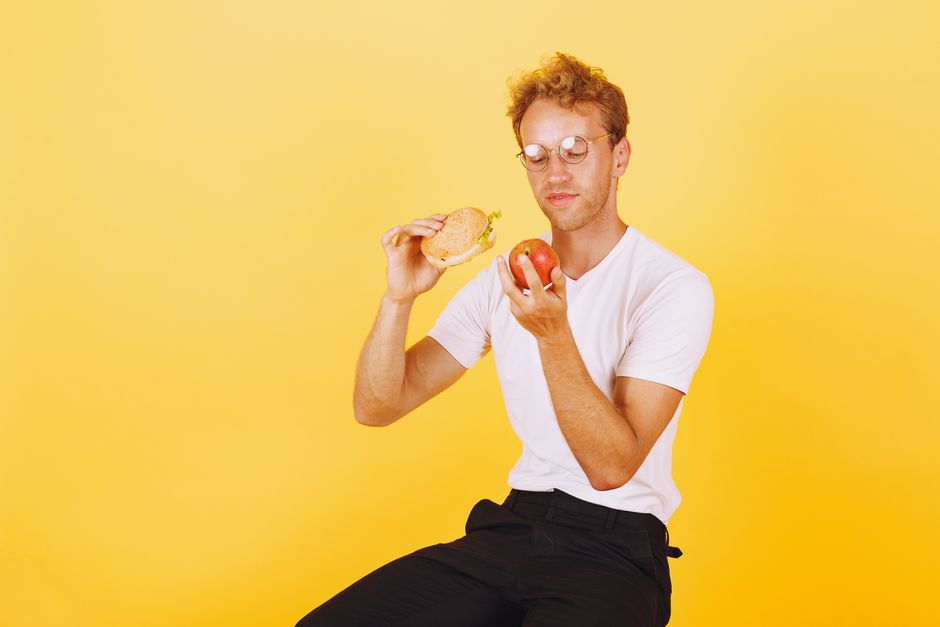 Man in white shirt holding a burger and apple on yellow background.