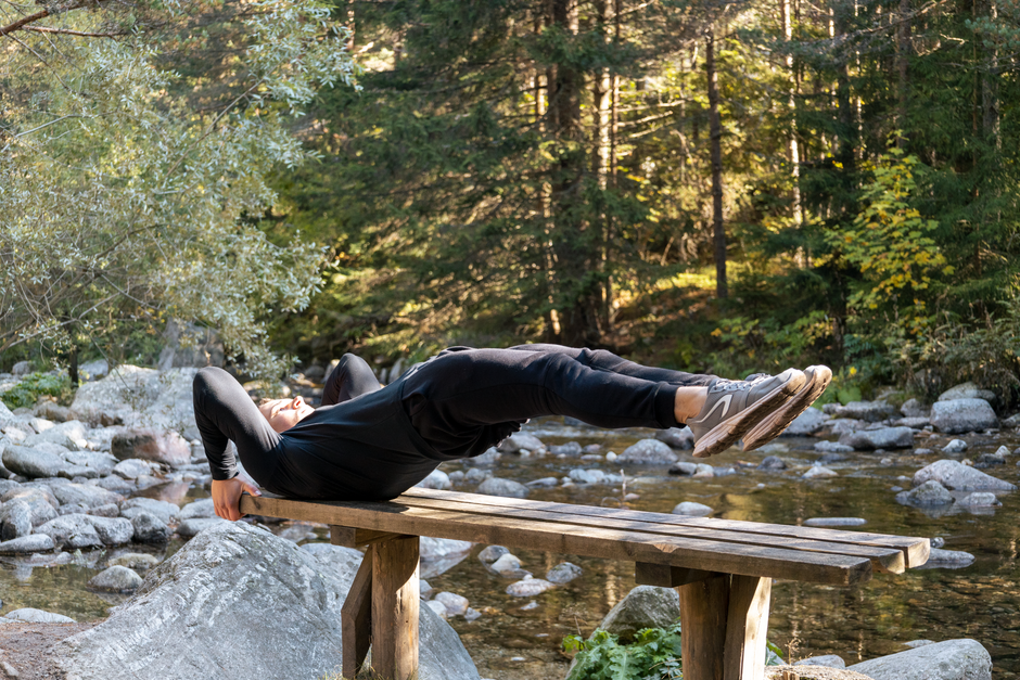 Man performing a core exercise on a bench by a serene river in a forest setting.