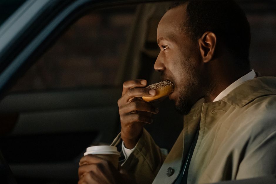 Man sitting in car enjoying a donut and coffee, captured in a casual and candid moment.