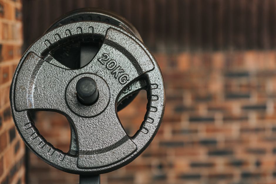 Modern black dumbbell with circle shaped plates indicating weight number on solid surface in daylight