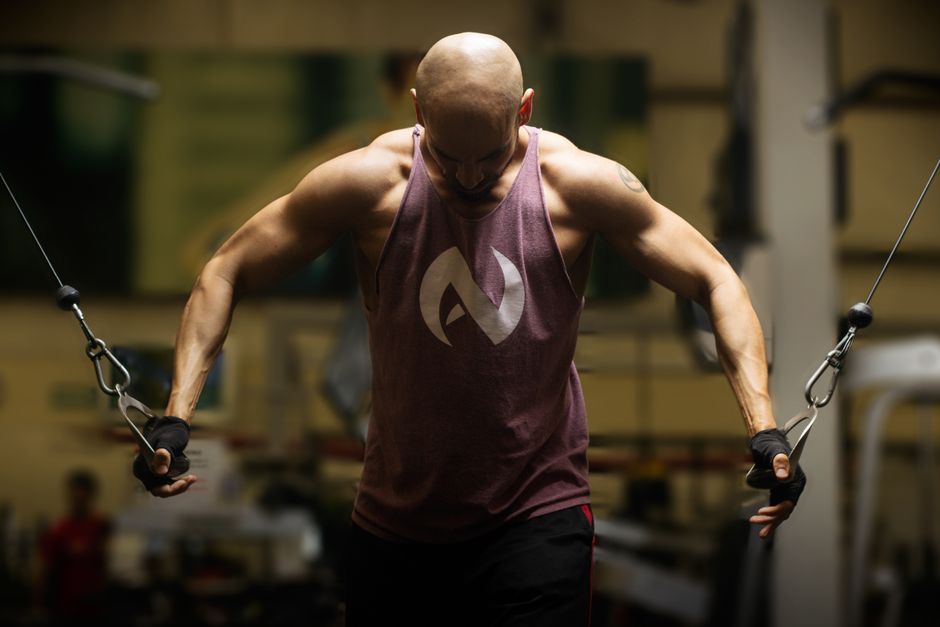 Muscular bald man performing cable workout in gym, focusing on fitness and strength.