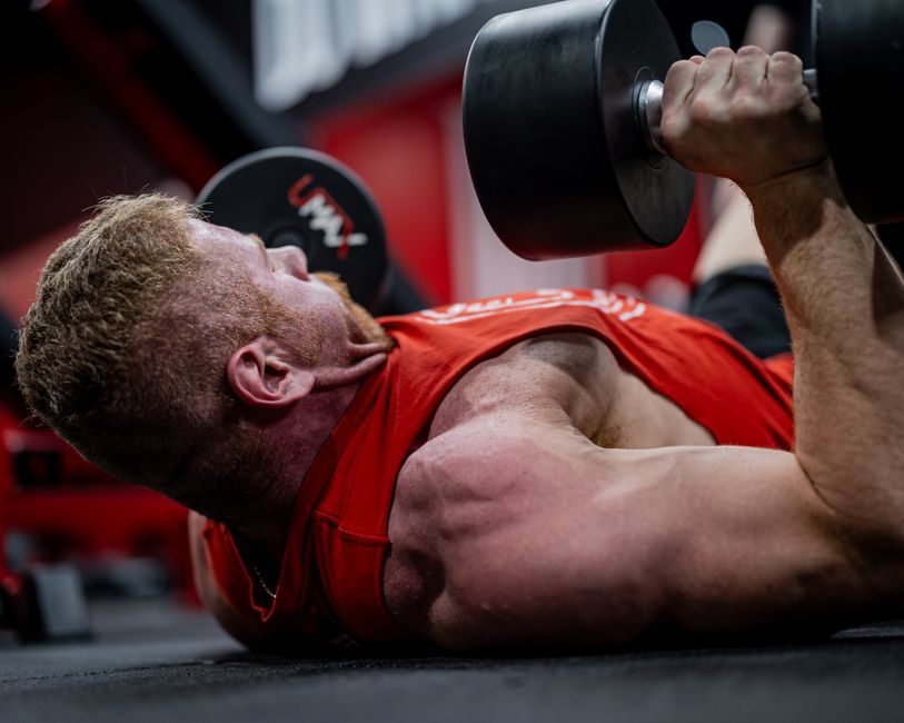 Muscular man performing a dumbbell press workout, focusing on strength and endurance.