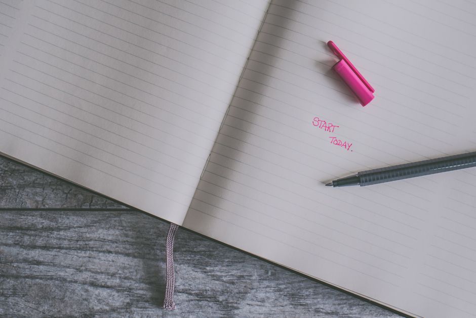 Open lined notebook with a pink highlight and pen on a wooden surface, inspiring writing theme.