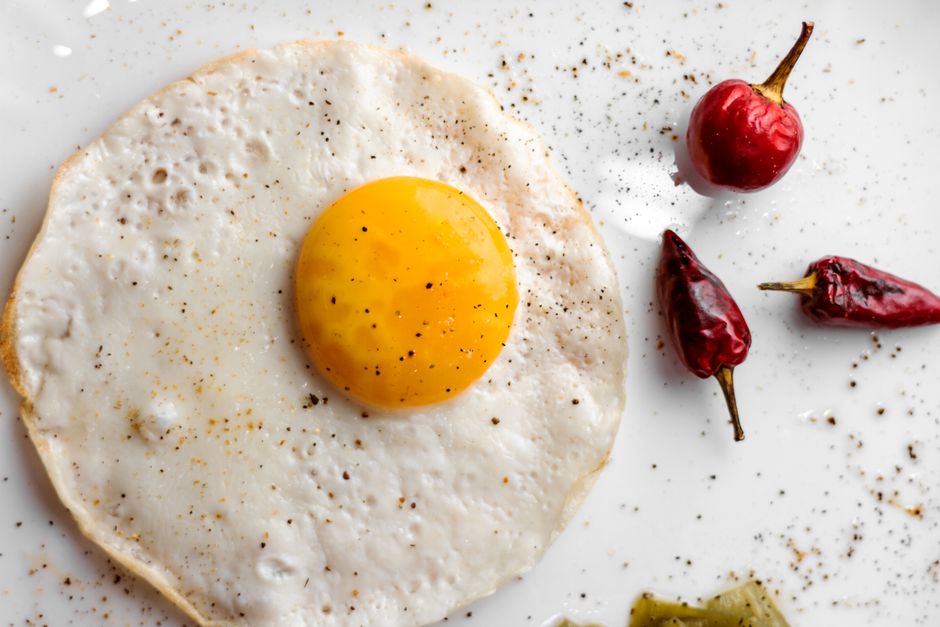 Overhead shot of a sunny side up egg with vibrant chilis on a white plate.