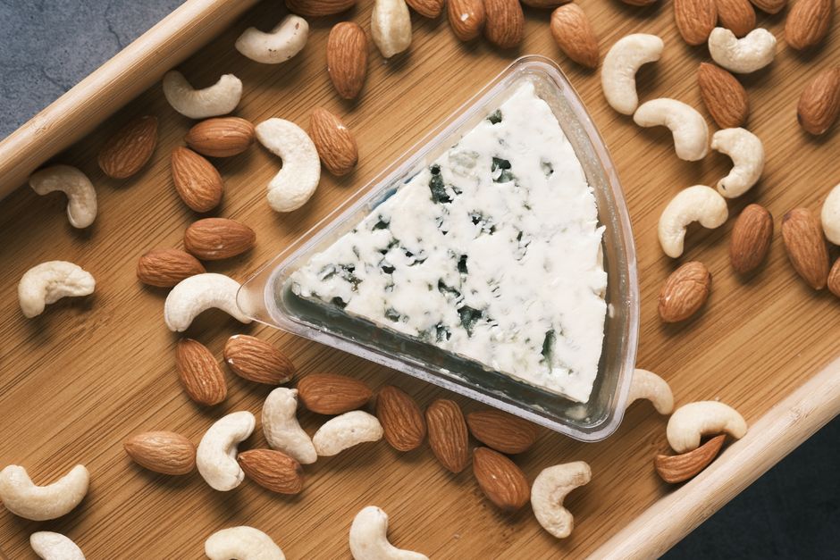 Overhead shot of triangle blue cheese surrounded by almonds and cashews on a wooden board.