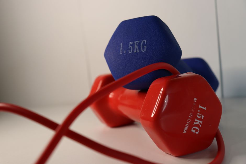 Pair of vibrant dumbbells with a red skipping rope on a white surface, perfect for home workouts.