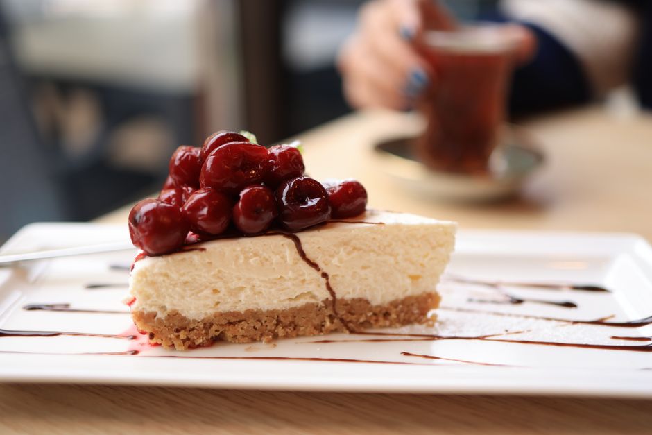 Scrumptious slice of cheesecake topped with cherries on a white plate in a cozy setting.