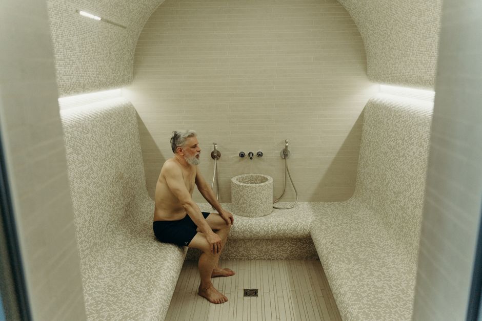 Senior man enjoying relaxation in a modern sauna, sitting shirtless and calm.