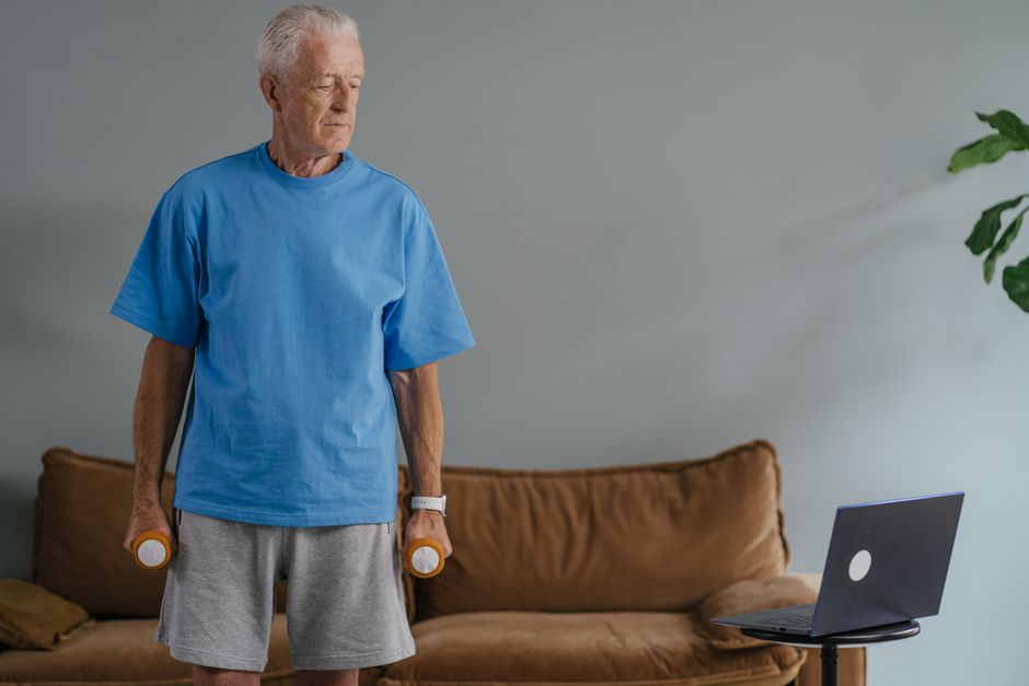 Senior man lifting dumbbells at home, staying fit with an online workout session.