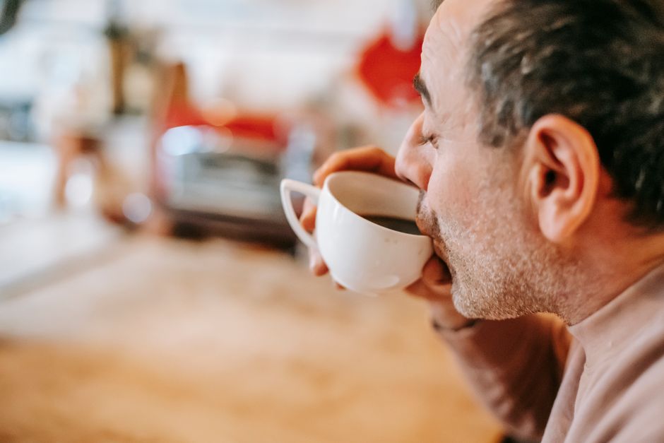 Side view of crop middle aged ethnic male drinking aromatic hot coffee with closed eyes during breakfast at home