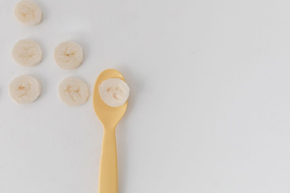 Sliced bananas on white background with a stylish gold spoon for a minimalistic look.