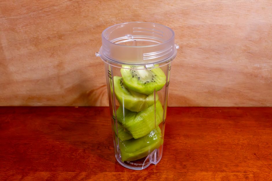 Sliced kiwi stacked inside a clear blender cup on a wooden table.