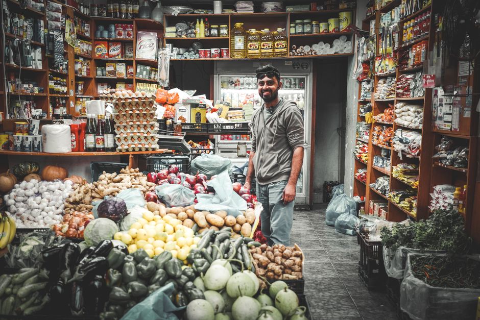 Smiling man in Athenian grocery store surrounded by colorful fruits and vegetables.
