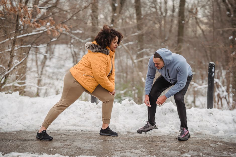 Sporty young coach helping plus size African American woman with warming up in winter forest