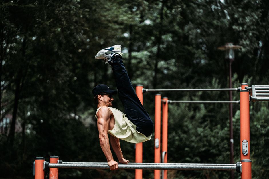 Strong man executes handstand on outdoor bar, showcasing athletic muscles.