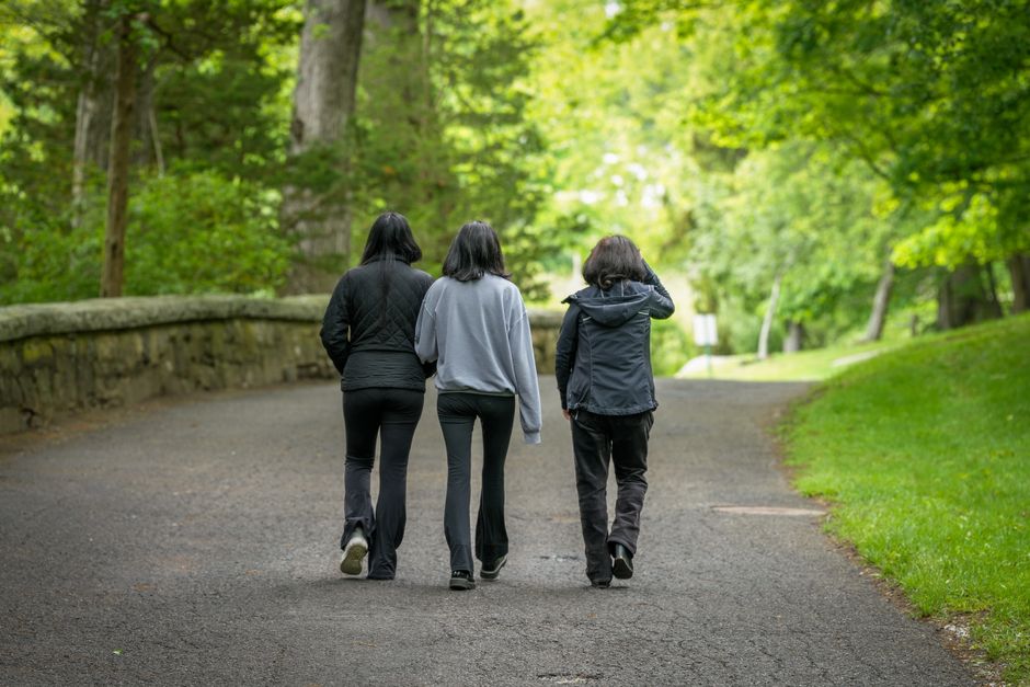 Three people walk together on a scenic path in Darien, Connecticut, surrounded by lush greenery.