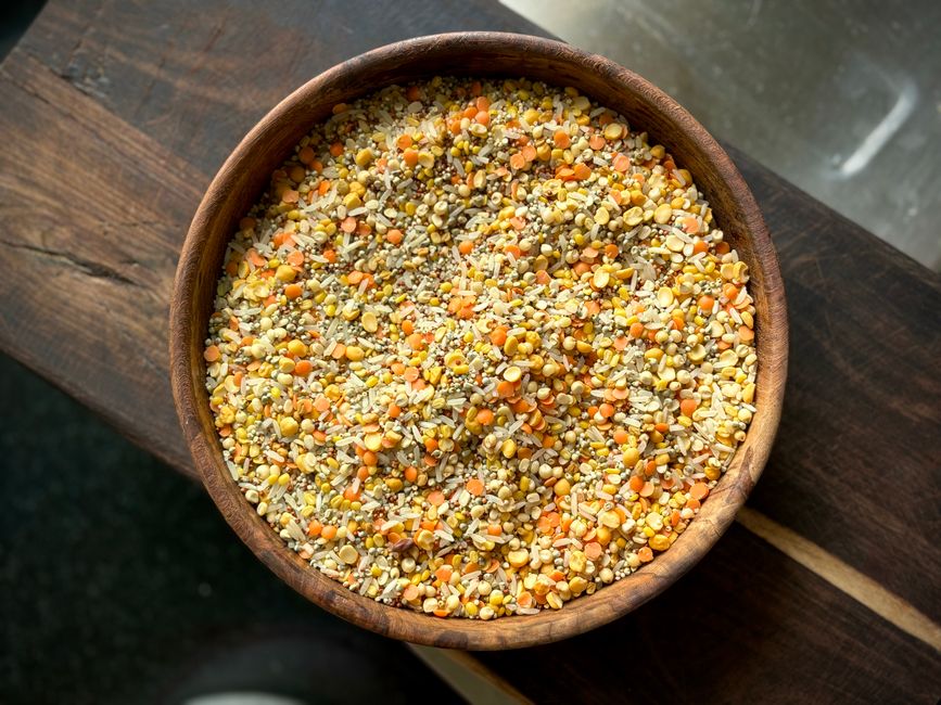 Top-down view of a wooden bowl filled with mixed millets and lentils on a wooden table.