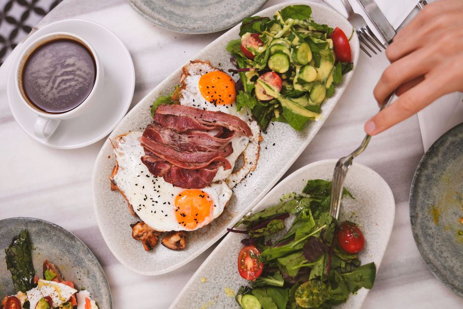Top view of a brunch meal featuring fried eggs, bacon, fresh salad, and coffee.