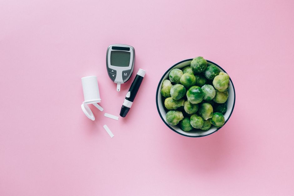 Top view of a glucometer and fresh Brussels sprouts on a pink background promoting health.