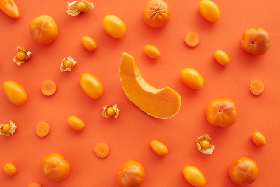 Top view of assorted orange fruits and vegetables on orange surface, offering organic health benefits.