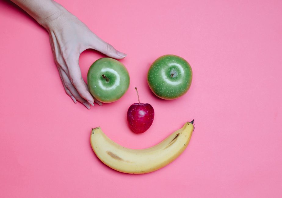Top view of crop anonymous female making smiling face out of apples and banana on pink background